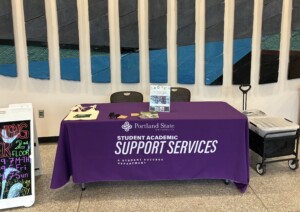 A table and chairs in the entrance lobby of the Portland State Library. The tablecloth has the logo for Portland State University Student Academic Support Services.