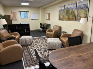 A room with four leather armchairs, two tables, a small bookshelf, and a desk.