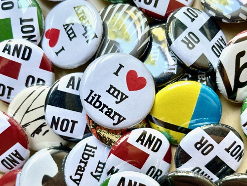 A pile of novelty buttons with library-related messages like 'I heart my library' and 'And Or Not'.